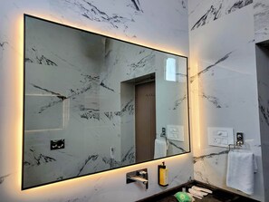 A bathroom with a large mirror, marble walls, a towel rack, and a soap dispenser.