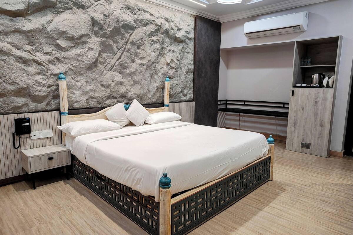 A modern bedroom with a large bed, a nightstand, a wardrobe, and an air conditioning unit.