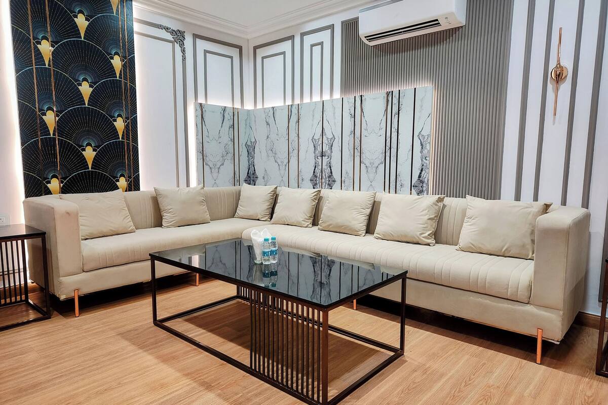 A modern living room with a beige sectional sofa, a glass coffee table, and a patterned wallpaper.