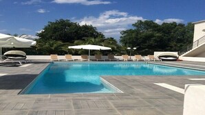 Une piscine rectangulaire, bordée d’une terrasse carrelée, entourée de chaises longues et de parasols.