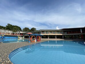 A swimming pool with a tiled deck, a covered seating area, and a building with multiple balconies in the background. - Paradise Adventure Camp 3 & Resort by Cocotel (San Jose del Monte)