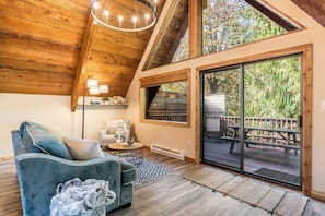 A cozy loft-style room with a wooden ceiling, a blue sofa, a small table, and a large sliding glass door leading to an outdoor deck.