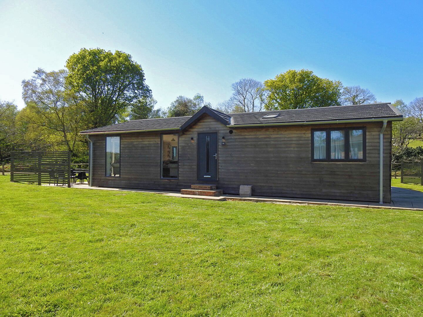 Een gelijkvloers huis met een donker houten gevel, een voordeur en een klein terras.