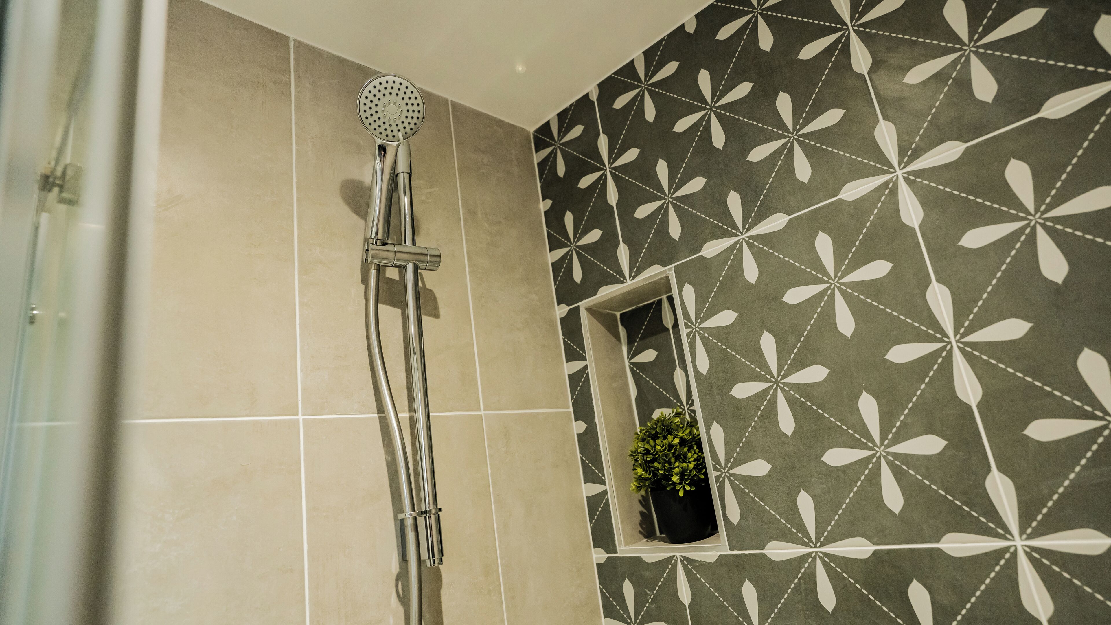 A shower with a handheld showerhead, a potted plant, and a decorative wall with a geometric pattern.