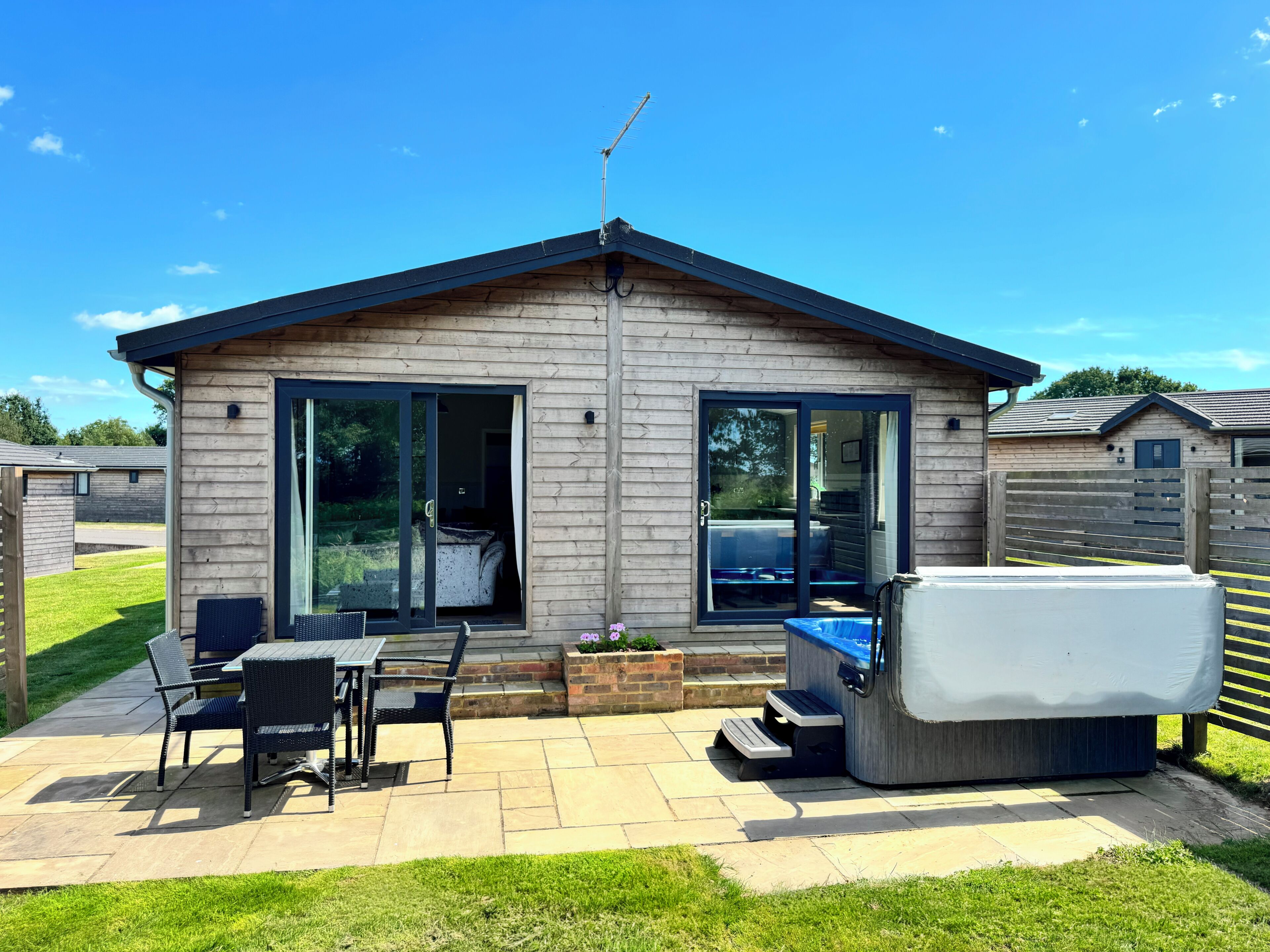 A small wooden cabin with a patio, sliding glass doors, and a covered hot tub.