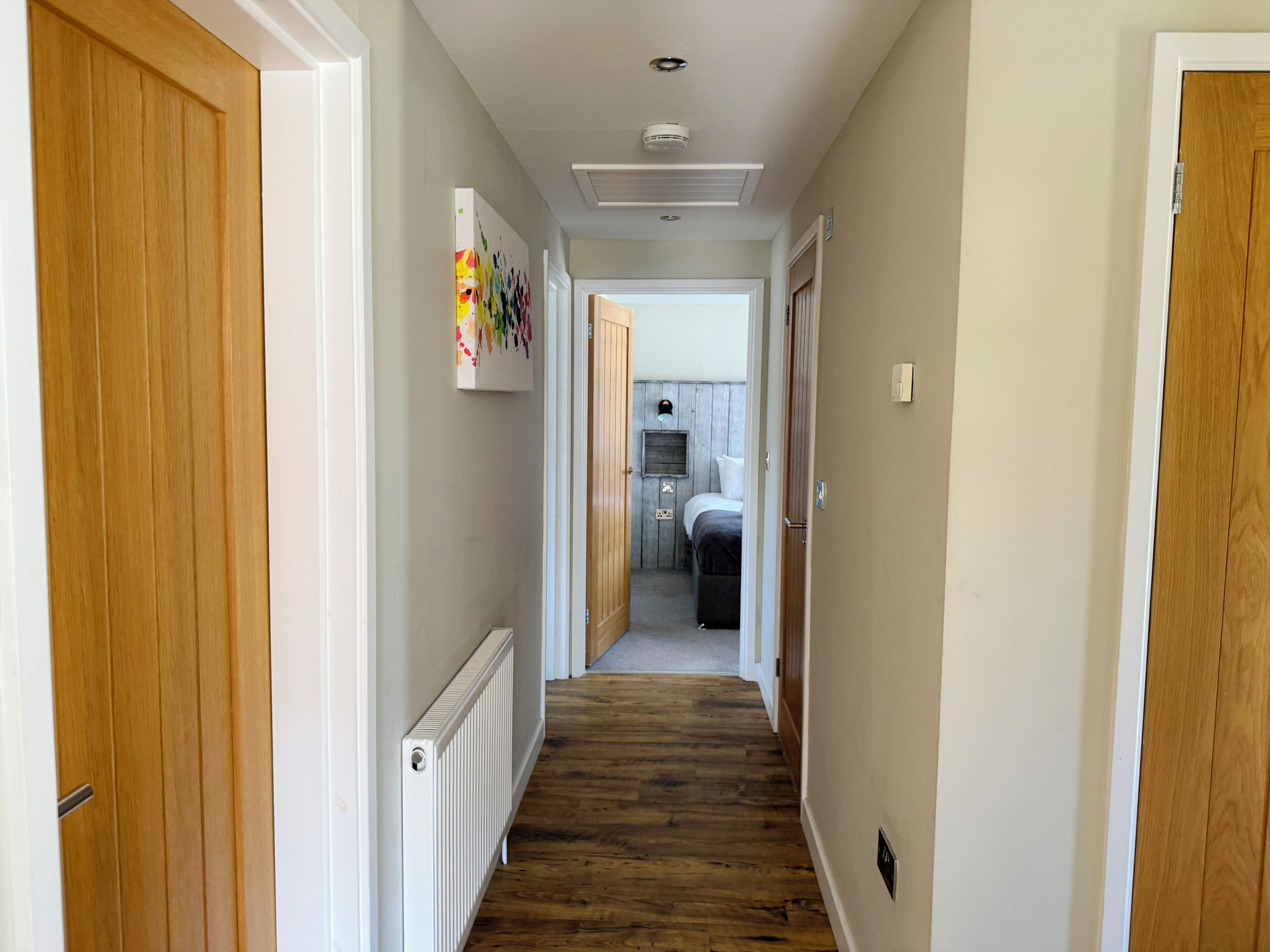 A hallway with wooden doors, a radiator, and a bed in the background.