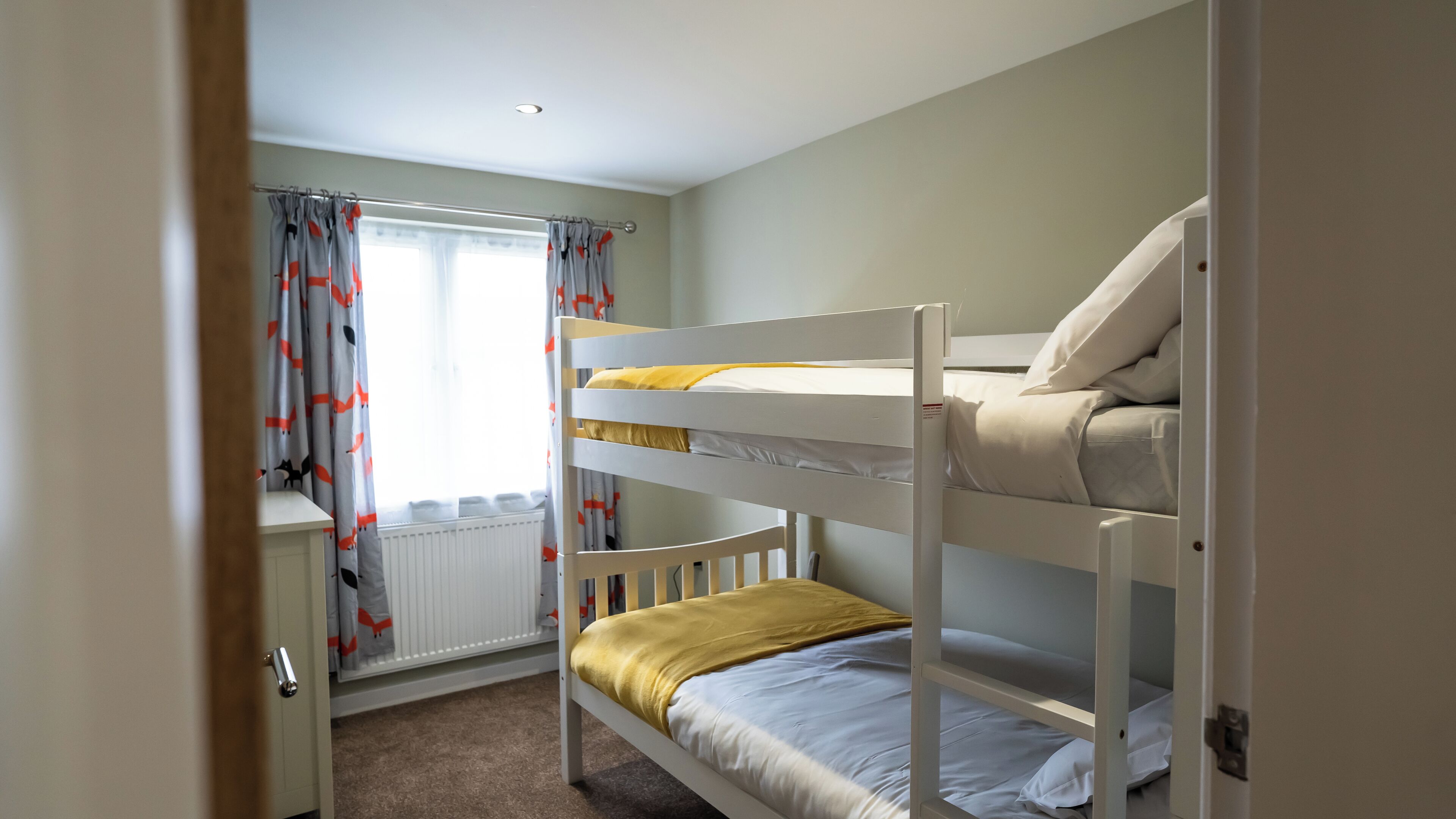 A bunk bed room with a radiator, curtains, and a door.