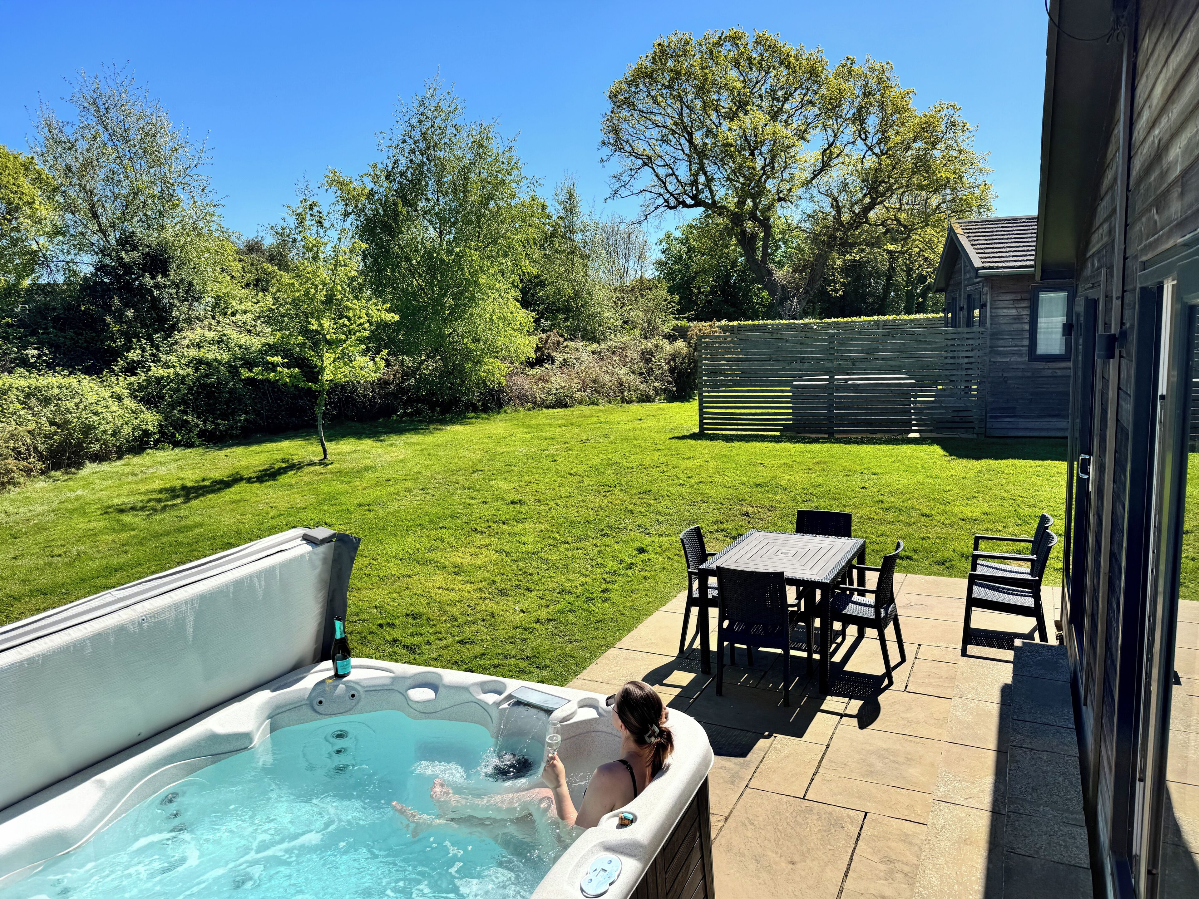 A backyard with a hot tub, a patio table, and chairs.