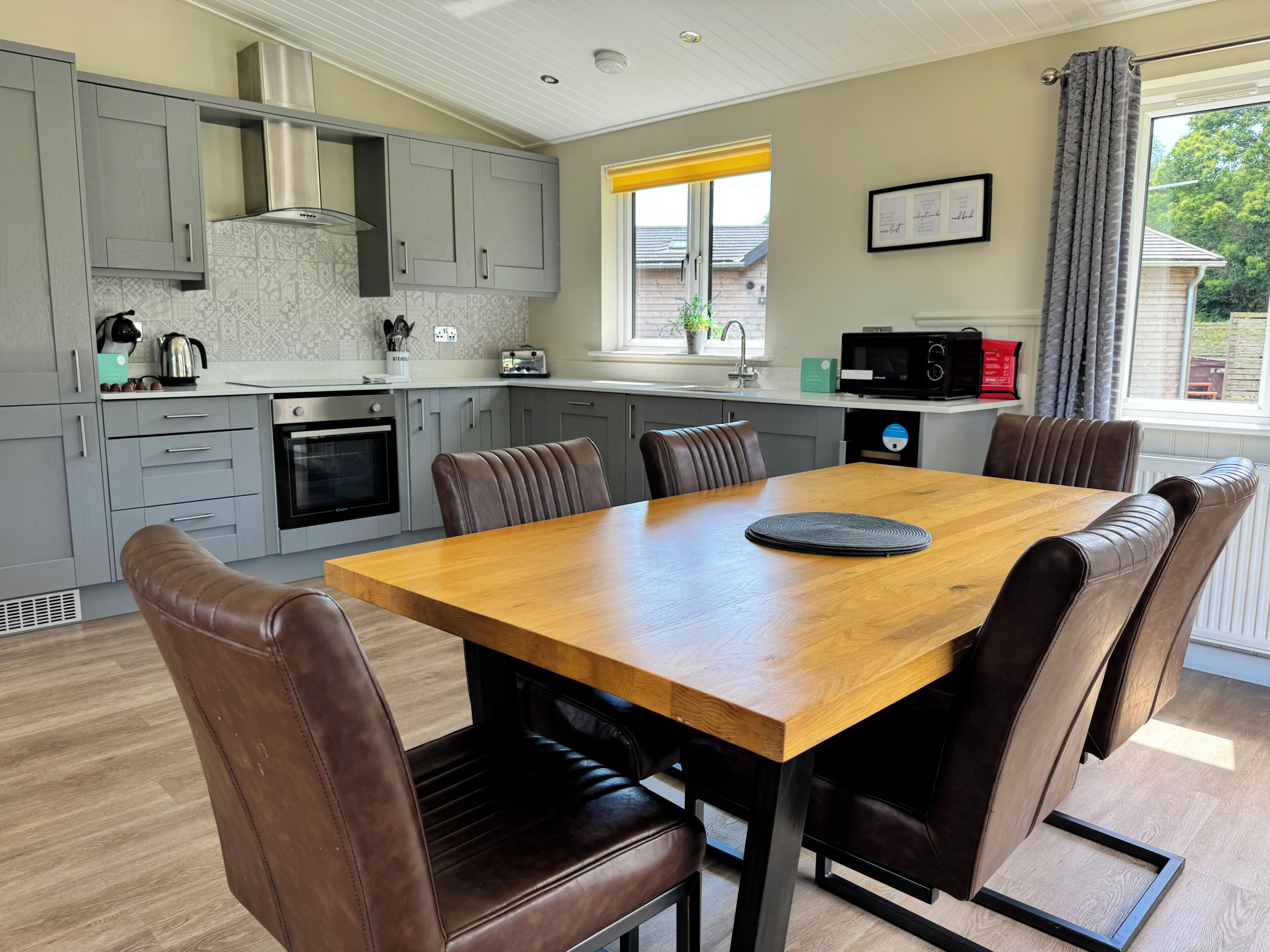 A modern kitchen with grey cabinets, a wooden dining table, and six brown leather chairs.