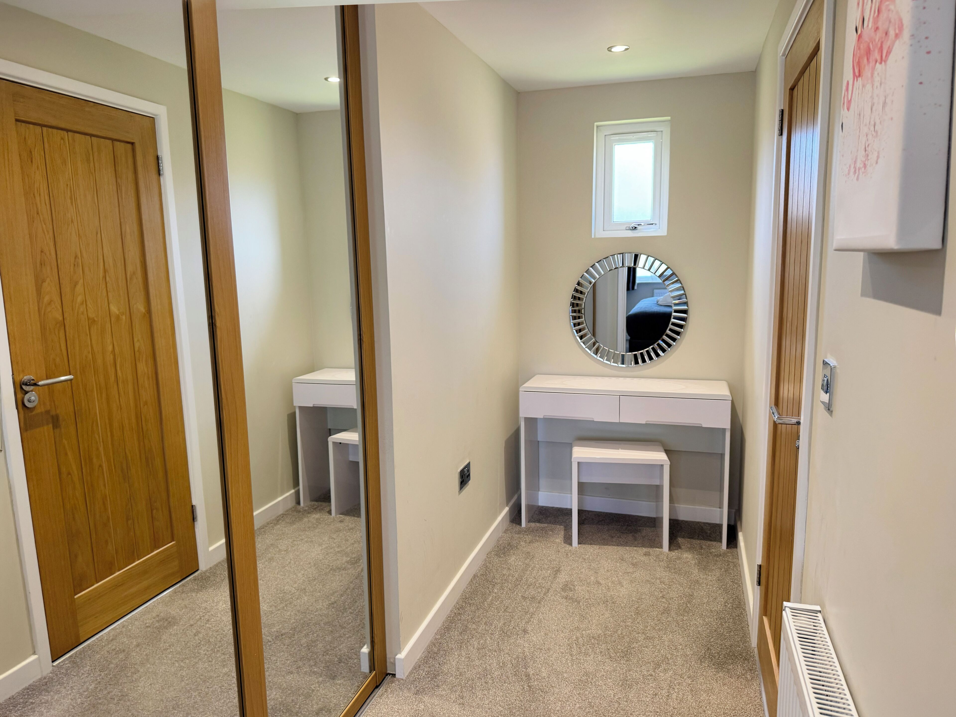 Un couloir avec une porte en bois, une coiffeuse blanche avec un miroir et un radiateur.