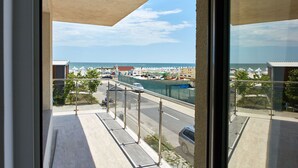 Ein Balkon mit Meerblick, eine Straße mit Fahrzeugen und ein eingezäunter Bereich mit Booten.