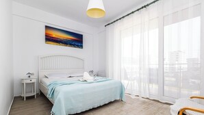 Ein Schlafzimmer mit Bett, Nachttisch, Stuhl, einem Fenster mit Vorhängen und einem Bild an der Wand.