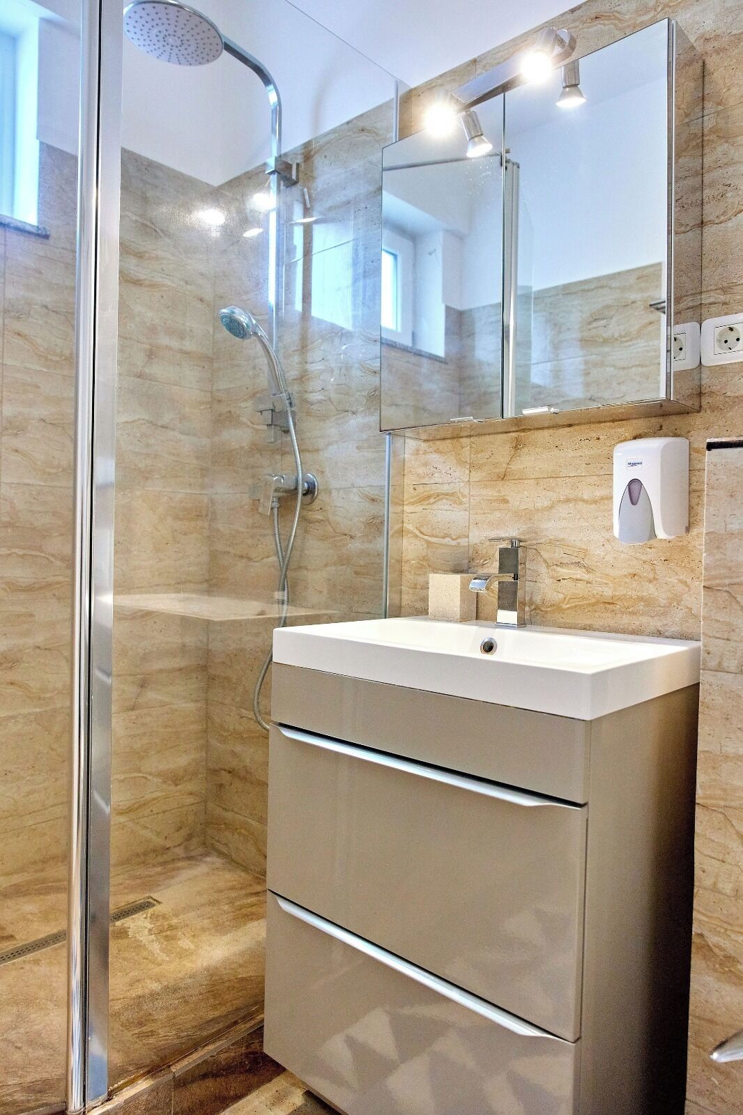 A modern bathroom with a glass-enclosed shower, a vanity with a mirror, and a soap dispenser.
