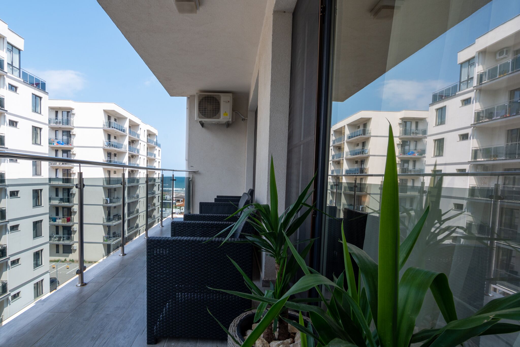 Un balcon donnant sur les bâtiments voisins, une plante en pot et un canapé en osier noir.