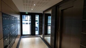 A hallway with a row of lockers on the left, a door on the right, and a view of the outside through a glass door. - Cosy, comfortable apartment in the city center (Caen)