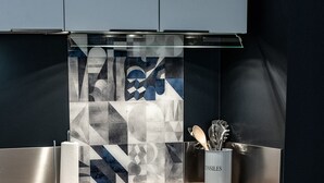 A modern kitchen with a geometric backsplash, stainless steel appliances, and a dining area with a round table set for two. - Cosy, comfortable apartment in the city center (Caen)