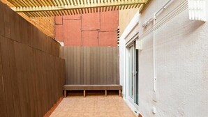 Un étroit couloir extérieur avec un banc en bois, un sol carrelé et un plafond en pente.