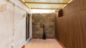Un étroit couloir extérieur, doté d’un sol carrelé, d’une clôture en bois d’un côté et d’un mur de pierre de l’autre.