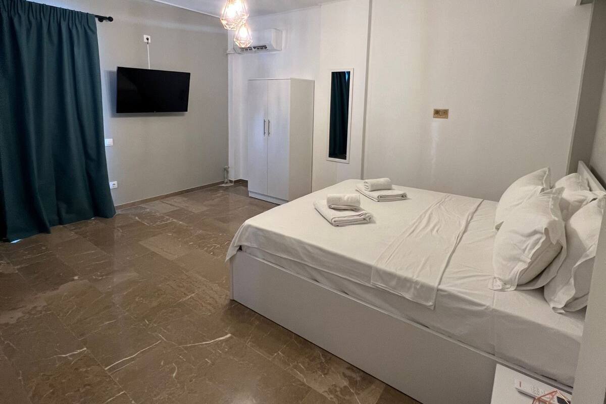 A bedroom with a bed, a TV, a wardrobe, and a desk with a lamp.