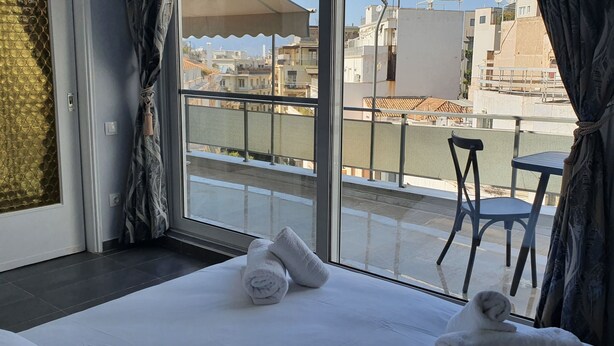 Habitación de hotel con un ventanal grande, una cama con ropa de cama blanca, una silla y vistas a la ciudad.