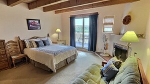 A bedroom with a bed, a sofa, a wooden dresser, a desk, a chair, a window, and a door leading to an outdoor area. - Spacious, Well Stocked Condo in the Foothills (Valdez)