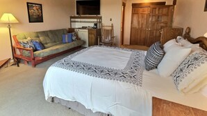 A bedroom with a large bed, a wooden ceiling, a sofa, a TV, and a door. - Spacious, Well Stocked Condo in the Foothills (Valdez)