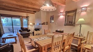 A cozy living room with a wooden dining table, chairs, a sofa, and a fireplace. - Spacious, Well Stocked Condo in the Foothills (Valdez)