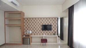A modern hotel room with a flat-screen TV mounted on a wall, a wooden wardrobe, a small table with a vase, and a compact refrigerator. - Cahaya 3 Hotel Near Juanda Airport (Sidoarjo)
