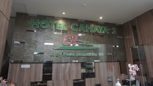 A reception desk with a sign for Hotel Cahaya 3, a logo, and a location marker. - Cahaya 3 Hotel Near Juanda Airport (Sidoarjo)