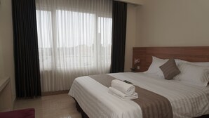 A hotel room with a large bed, a wooden headboard, a window with sheer curtains, and a red chair. - Cahaya 3 Hotel Near Juanda Airport (Sidoarjo)