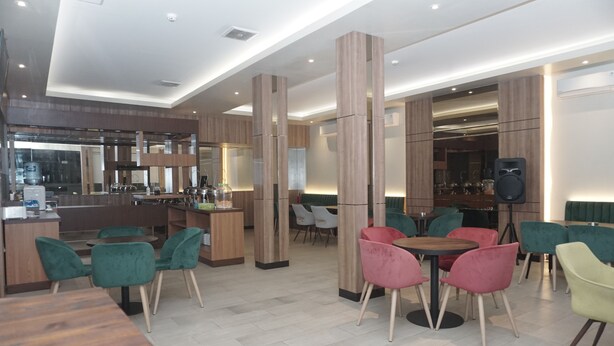 A modern restaurant with wooden accents, green and pink chairs, and a bar area. - Cahaya 3 Hotel Near Juanda Airport (Sidoarjo)