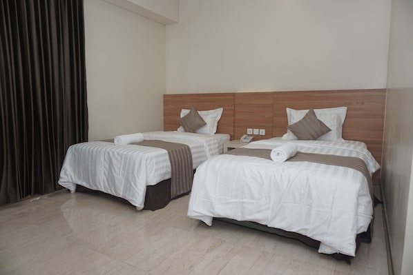 A hotel room with two single beds, each with a wooden headboard, white bedding, and a brown throw blanket.