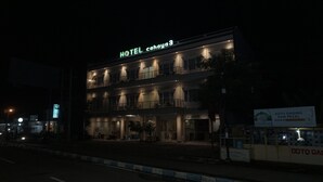 A multi-story hotel with illuminated signage, a balcony on the second floor, and a signboard advertising a nearby service. - Cahaya 3 Hotel Near Juanda Airport (Sidoarjo)
