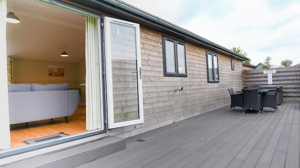 Une façade en bois avec une porte-fenêtre coulissante donnant sur une pièce où se trouve un canapé gris.