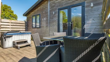 A wooden deck with outdoor furniture, a hot tub, and a sliding glass door to a covered patio.