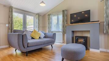 A modern living room with a sofa, ottoman, fireplace, television, and large windows.