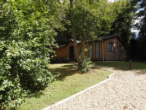 Une cabane en bois, accessible par un chemin de gravier, entourée d’un feuillage verdoyant et luxuriant.