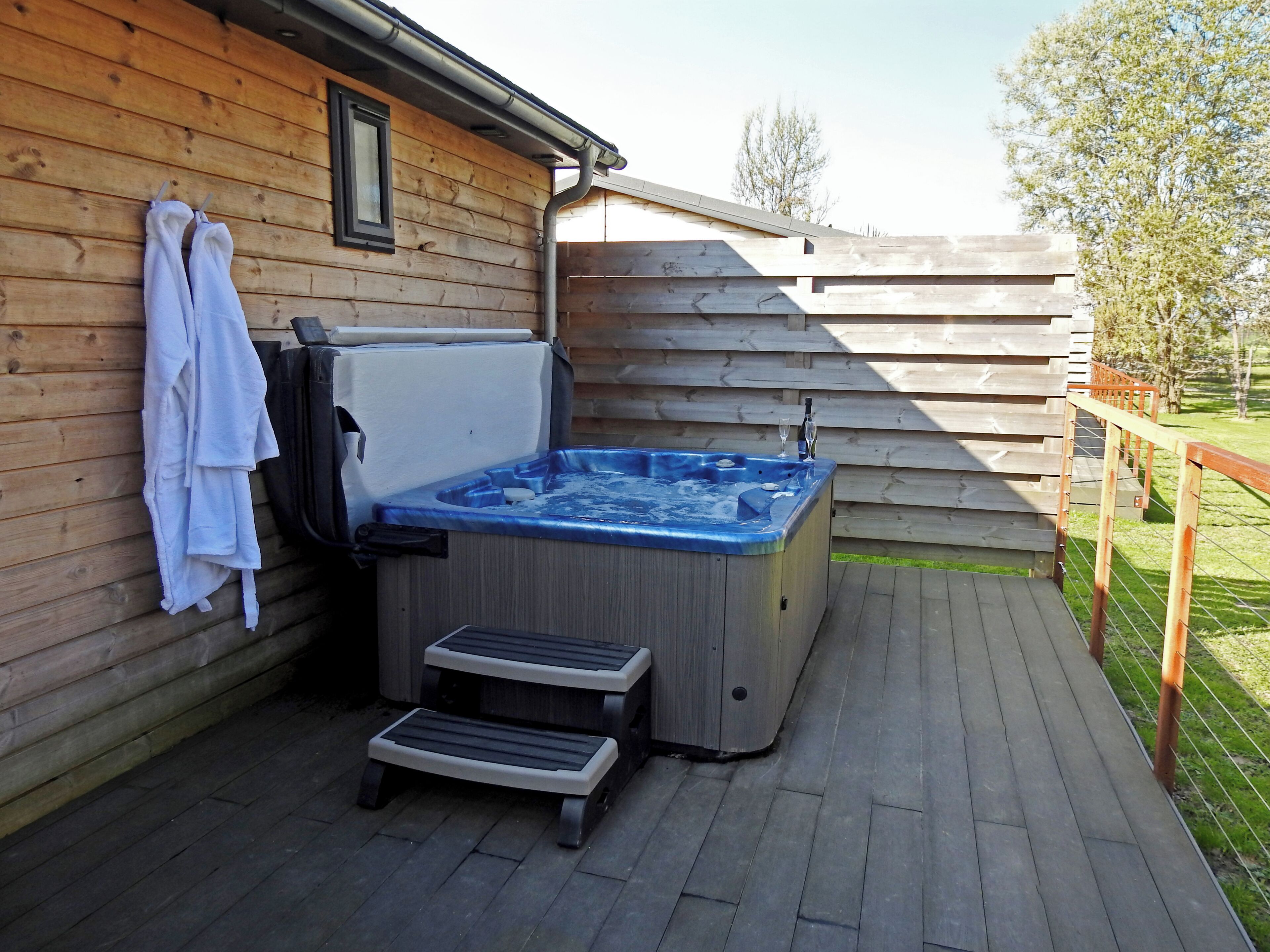 Een houten terras met een jacuzzi, een opstapje en een handdoekhouder.
