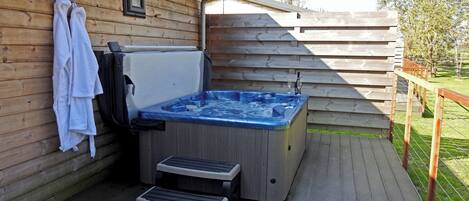 A wooden deck with a hot tub, a step stool, and a towel rack.