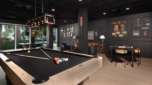 Una mesa de billar con bolas, una zona de estar con sillones y una pared con cuadros enmarcados y un cartel.