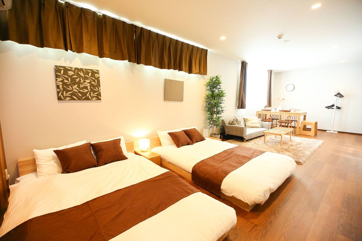 A hotel room with two beds, a desk, a chair, a plant, and a sofa.