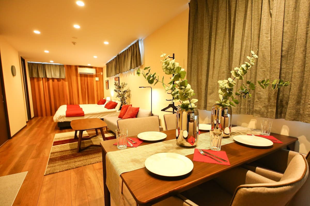A hotel room with a dining area, a sofa, a bed, and a plant.