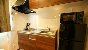 A compact kitchen with wooden cabinets, a stainless steel sink, and a black refrigerator. - Prime Room Beppu Root (Beppu)