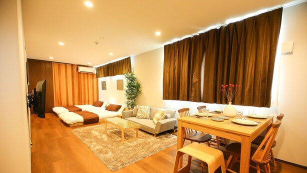 A modern living room with a sofa, a coffee table, and a dining table set for four. - Prime Room Beppu Root (Beppu)