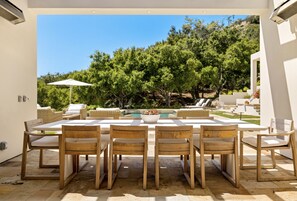 An outdoor patio with a pool, surrounded by lush greenery and white furniture.