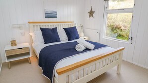 A neatly arranged bedroom with a wooden bed, white walls, a star decoration, and a window with a view of greenery. - Top Of The World Lodge (Aberdovey)