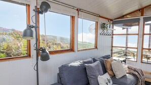 A cozy room with a grey sofa, multiple windows, and a view of greenery. - Top Of The World Lodge (Aberdovey)