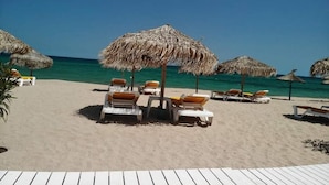 A beach with thatched umbrellas and lounge chairs.