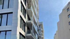 A multi-story residential building with balconies, a parking area, and a clear sky.