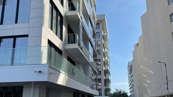 A multi-story residential building with balconies, a parking area, and a clear sky.